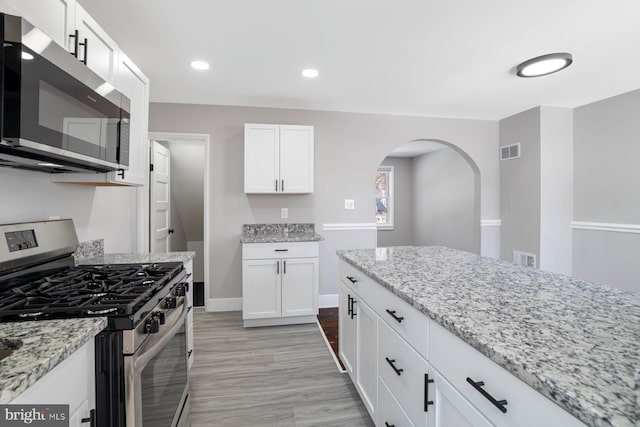 kitchen with light hardwood / wood-style flooring, stainless steel appliances, white cabinetry, and light stone counters