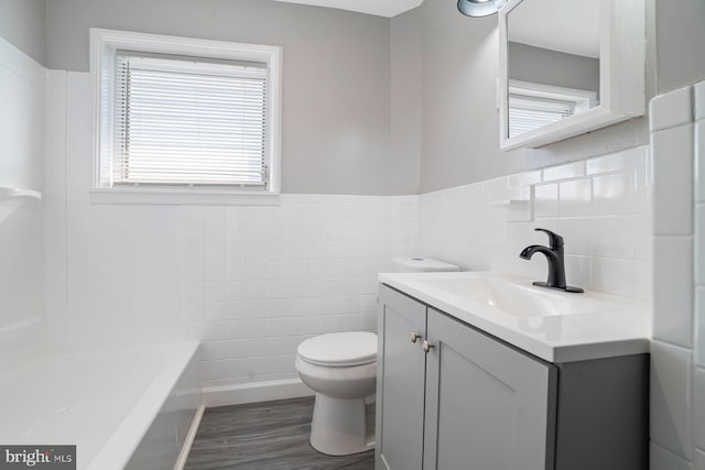 bathroom featuring vanity, hardwood / wood-style flooring, a washtub, toilet, and tile walls