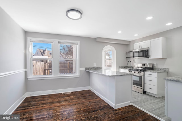 kitchen with dark wood-type flooring, white cabinets, stainless steel range with gas cooktop, light stone countertops, and kitchen peninsula