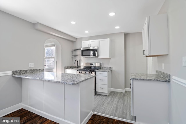 kitchen featuring kitchen peninsula, light stone countertops, white cabinets, and appliances with stainless steel finishes