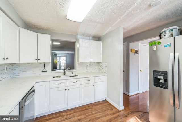 kitchen with appliances with stainless steel finishes, backsplash, sink, wood-type flooring, and white cabinets