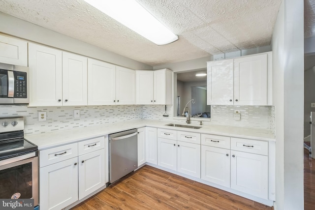 kitchen with light wood-type flooring, tasteful backsplash, stainless steel appliances, sink, and white cabinets