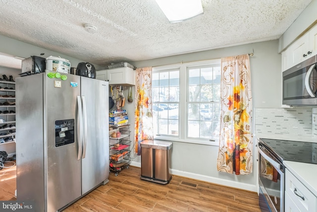 kitchen featuring tasteful backsplash, white cabinets, light wood-type flooring, and appliances with stainless steel finishes