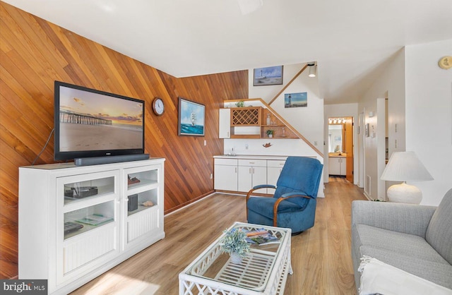 living room featuring bar, wood walls, and light wood-type flooring