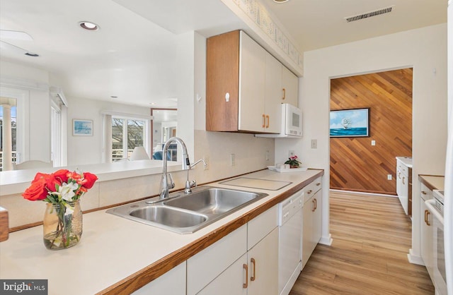 kitchen featuring white appliances, white cabinetry, wooden walls, sink, and light wood-type flooring