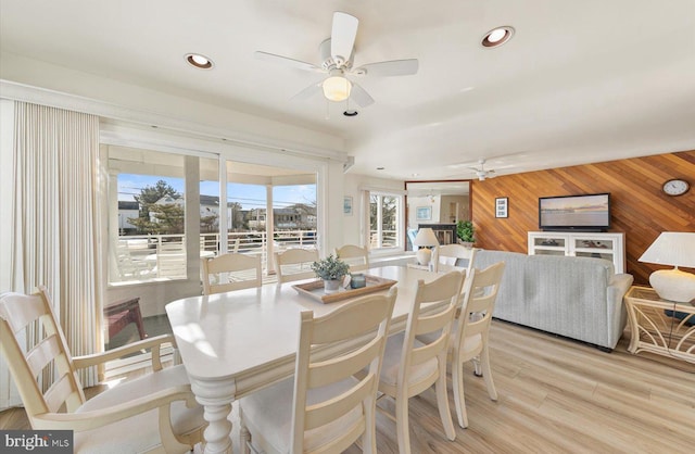 dining area featuring light wood-type flooring, ceiling fan, and wooden walls