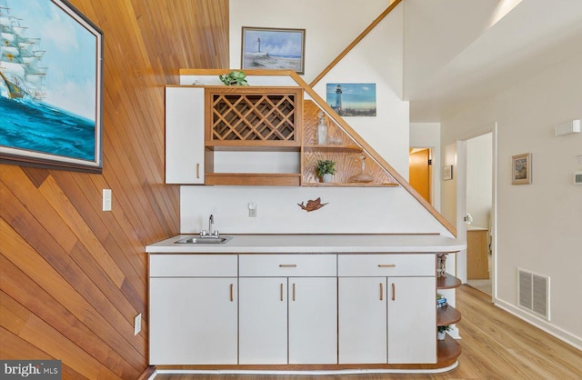 interior space with light hardwood / wood-style floors, sink, white cabinetry, and wood walls