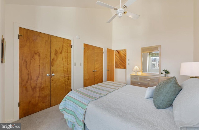 carpeted bedroom with multiple closets, high vaulted ceiling, and ceiling fan