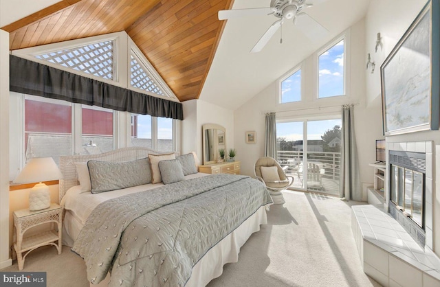 carpeted bedroom with ceiling fan, wood ceiling, high vaulted ceiling, a tiled fireplace, and access to exterior