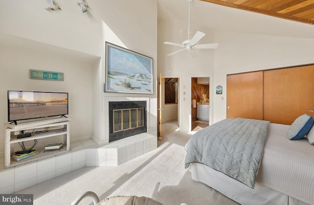 bedroom featuring ceiling fan, a tiled fireplace, light colored carpet, ensuite bath, and a closet