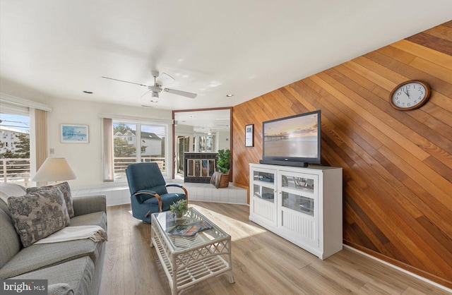 living room featuring ceiling fan, wood walls, light hardwood / wood-style flooring, and a wealth of natural light