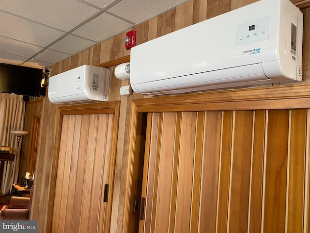 interior details featuring an AC wall unit, wood walls, and a drop ceiling