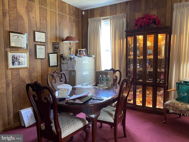 carpeted dining area featuring wood walls