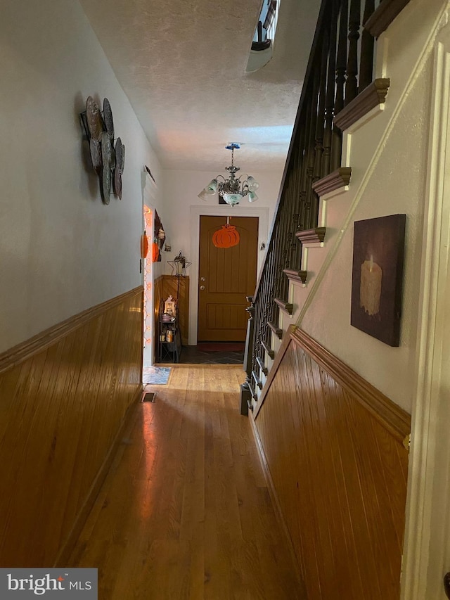 hallway featuring wooden walls, wood-type flooring, a textured ceiling, and an inviting chandelier