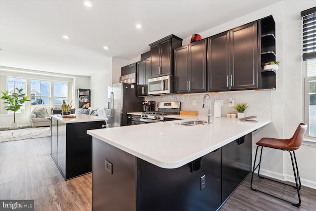 kitchen with a breakfast bar, sink, light hardwood / wood-style floors, kitchen peninsula, and stainless steel appliances