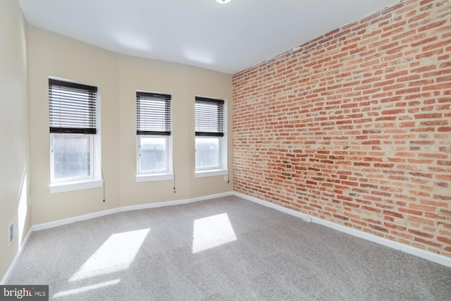 unfurnished room featuring brick wall, plenty of natural light, and carpet flooring