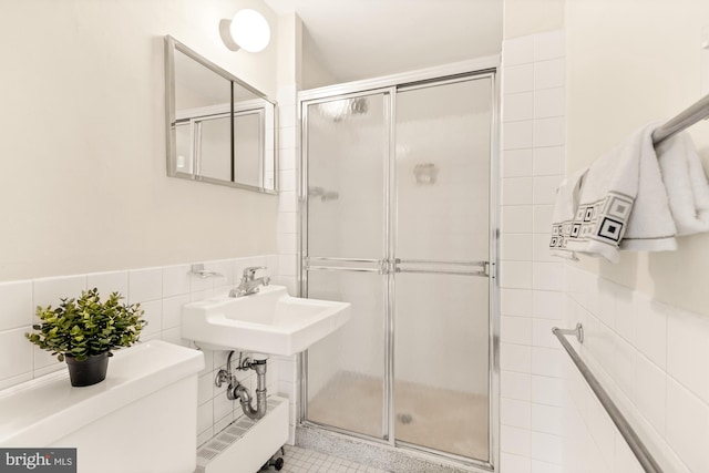 bathroom with sink, toilet, an enclosed shower, and tile walls