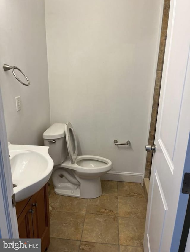 bathroom with toilet, stone finish flooring, baseboards, and vanity