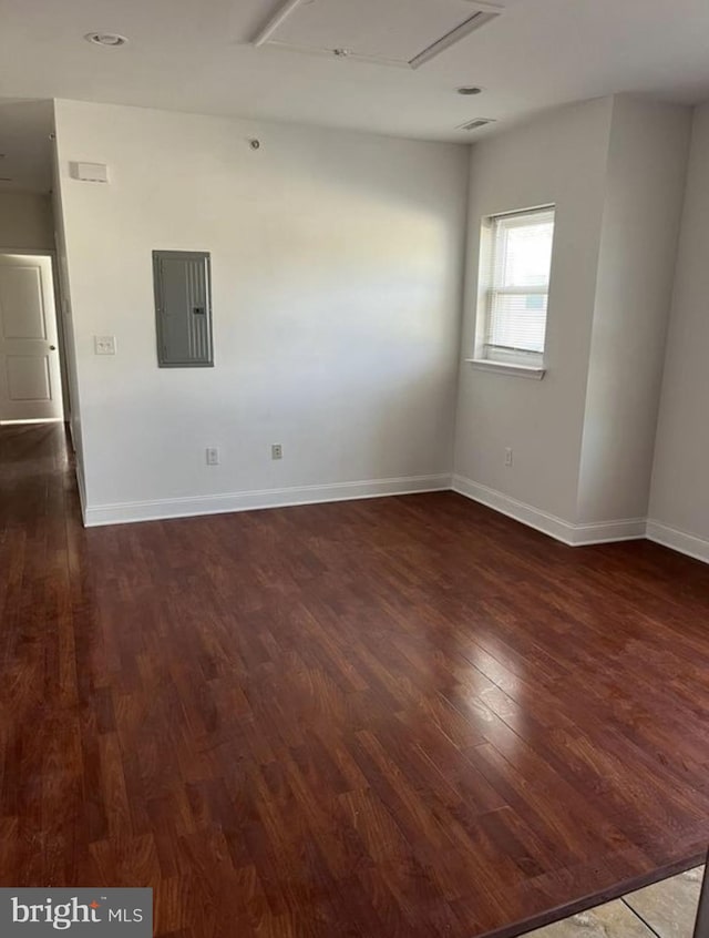 empty room with dark wood-style floors, electric panel, and baseboards