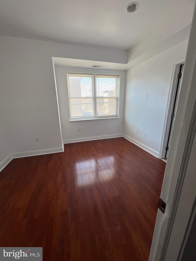 unfurnished room featuring dark wood-style floors, visible vents, and baseboards