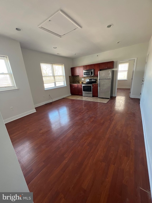 kitchen with stainless steel appliances, a healthy amount of sunlight, dark wood-type flooring, and tasteful backsplash