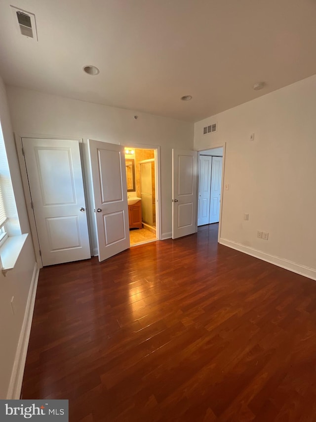 unfurnished bedroom featuring dark wood-style flooring, visible vents, ensuite bath, and baseboards