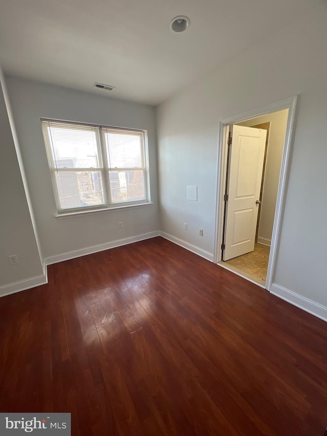 unfurnished room featuring baseboards, visible vents, and dark wood-style flooring