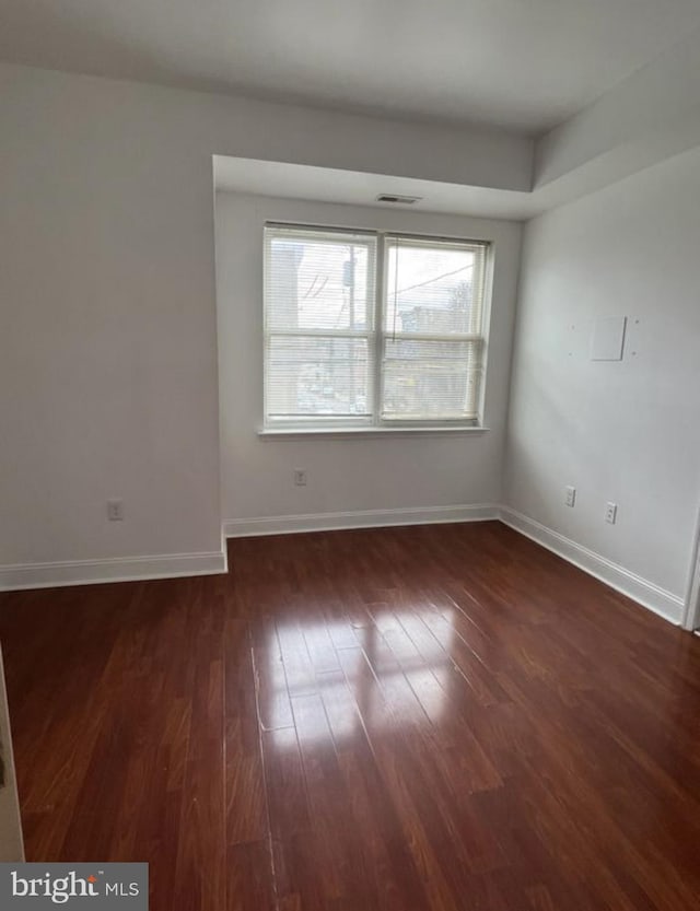 spare room featuring baseboards, visible vents, and dark wood-type flooring