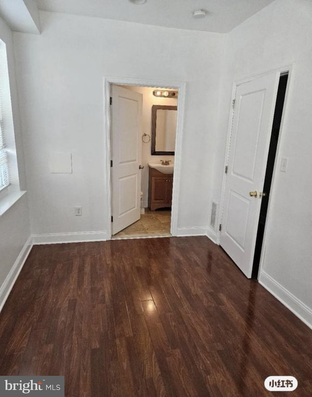 unfurnished bedroom with dark wood-style floors, connected bathroom, and baseboards