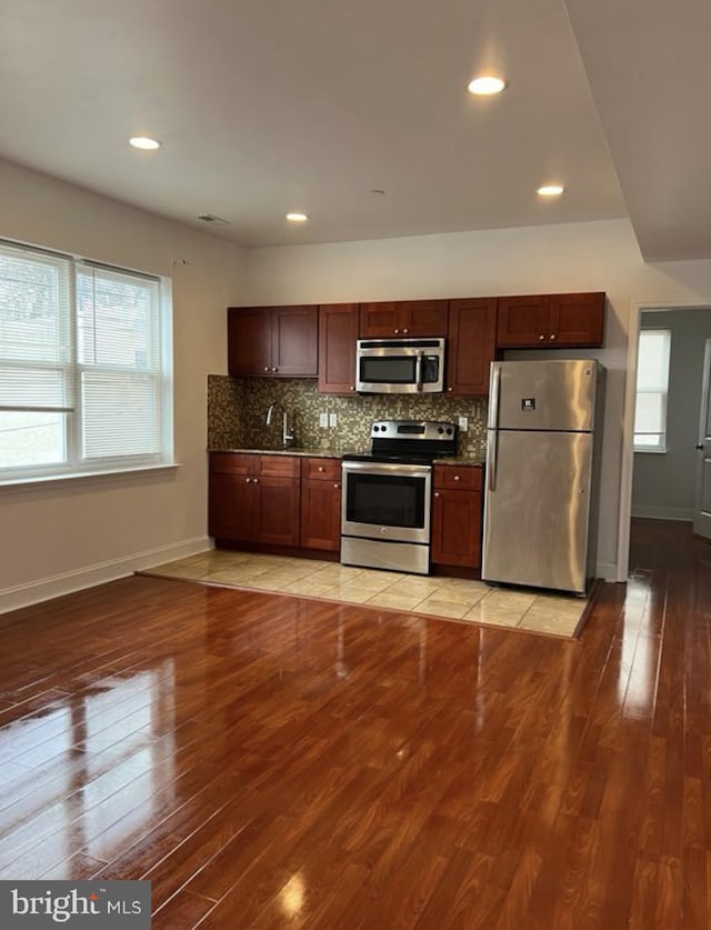 kitchen featuring light wood-style flooring, baseboards, stainless steel appliances, and backsplash