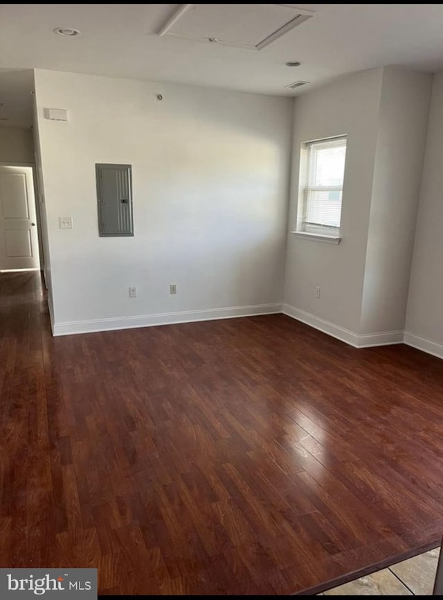 empty room featuring electric panel, dark wood finished floors, visible vents, and baseboards