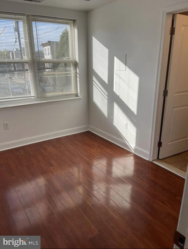 spare room with dark wood-style flooring, visible vents, and baseboards