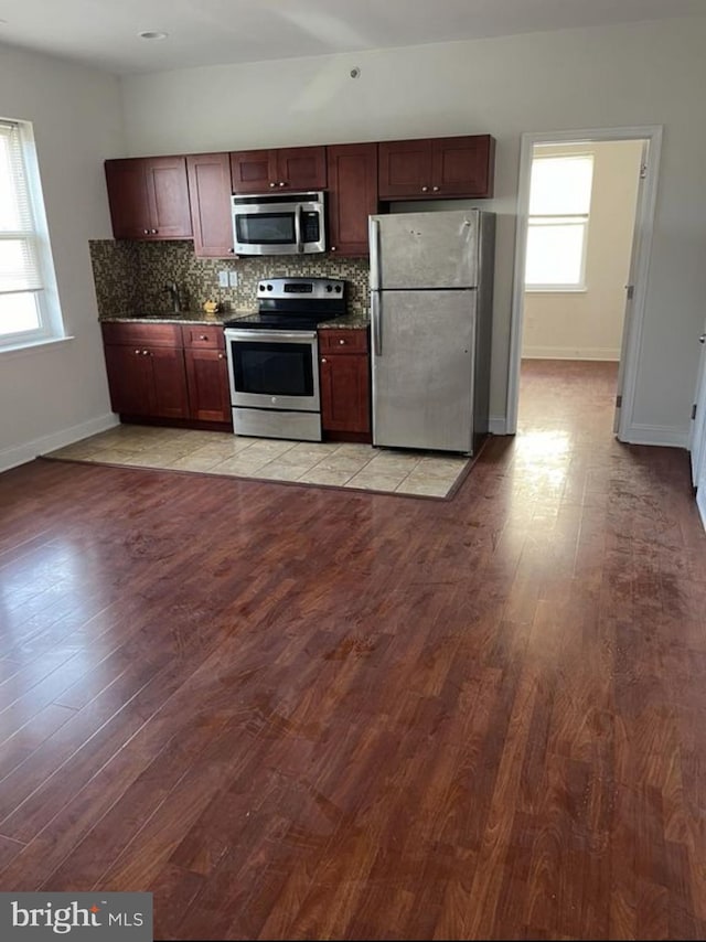 kitchen featuring tasteful backsplash, dark countertops, appliances with stainless steel finishes, light wood-type flooring, and baseboards