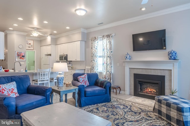 living room featuring sink, a tiled fireplace, ceiling fan, and crown molding