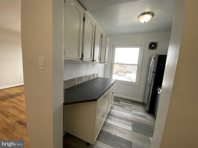 kitchen with stainless steel fridge, white cabinets, and light hardwood / wood-style floors