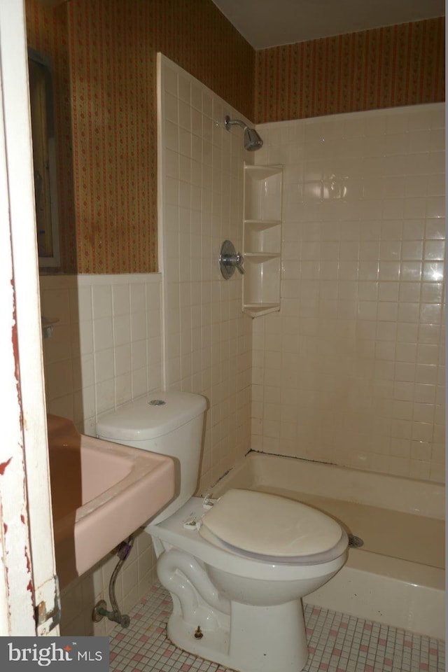 bathroom featuring tile patterned floors, a tile shower, tile walls, and toilet