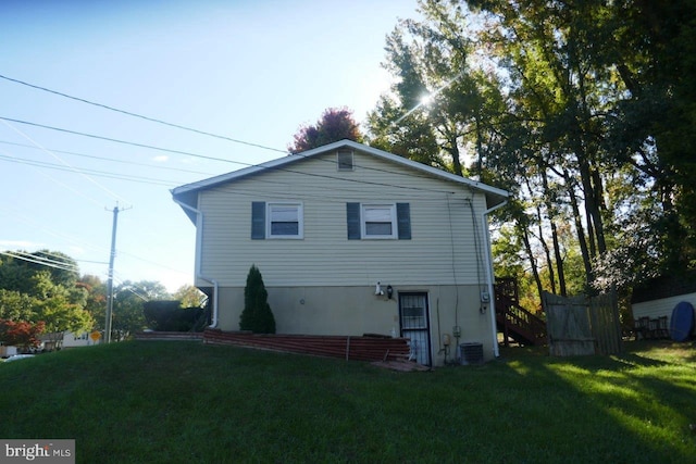 rear view of house featuring central AC unit and a lawn