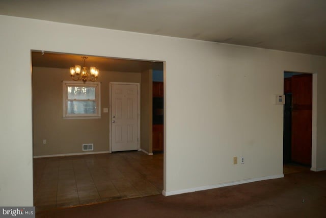 unfurnished room with a chandelier and dark tile patterned floors