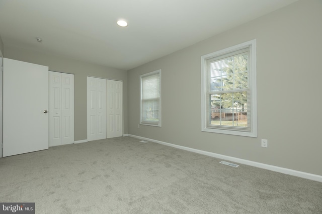 unfurnished bedroom featuring light colored carpet and multiple closets