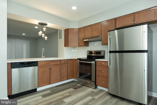 kitchen featuring pendant lighting, sink, light hardwood / wood-style flooring, appliances with stainless steel finishes, and kitchen peninsula