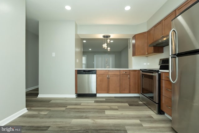 kitchen featuring kitchen peninsula, appliances with stainless steel finishes, sink, decorative light fixtures, and light hardwood / wood-style floors