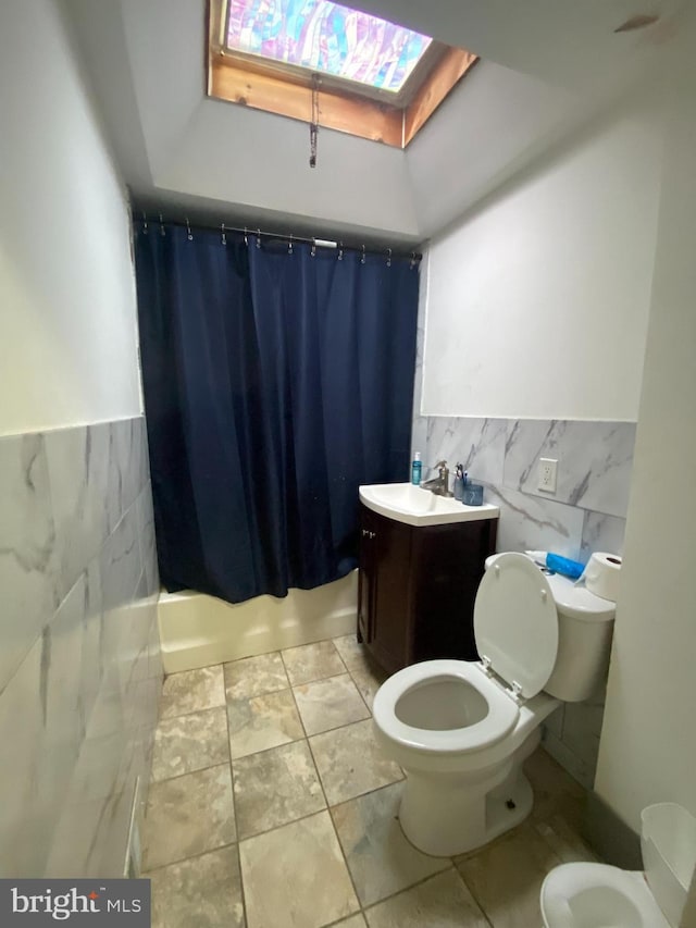 full bathroom featuring vanity, a skylight, toilet, and tile walls