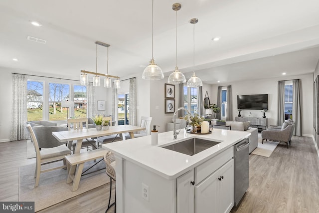 kitchen with a kitchen island with sink, sink, decorative light fixtures, white cabinets, and light hardwood / wood-style floors