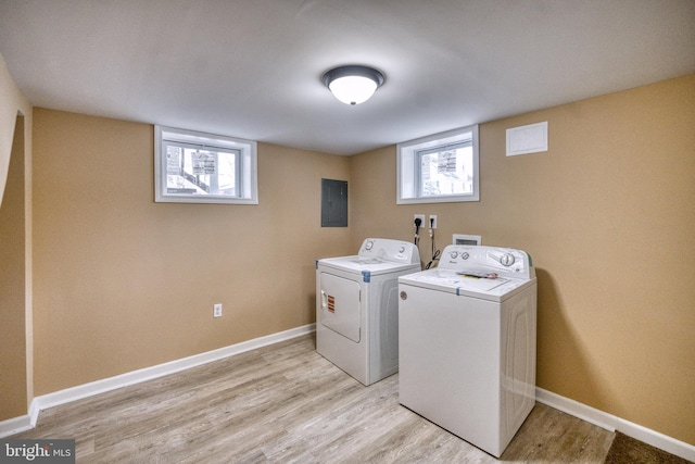 laundry area with electric panel, a wealth of natural light, light hardwood / wood-style floors, and washer and dryer