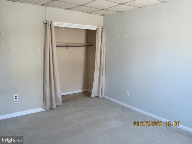 unfurnished bedroom with carpet, a drop ceiling, and a closet