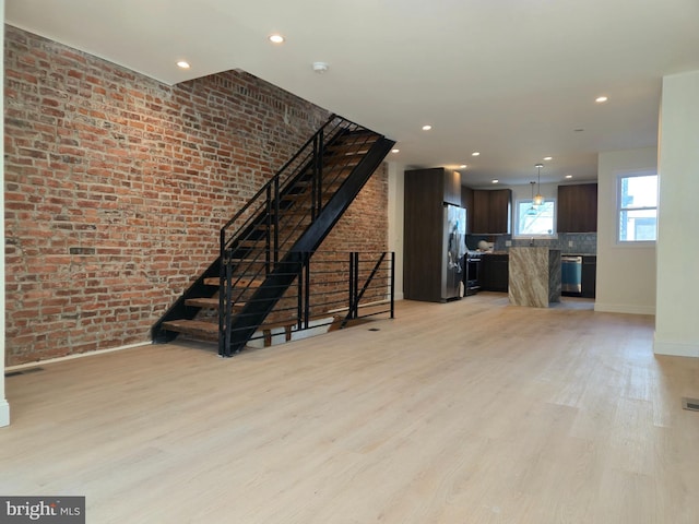 unfurnished living room featuring stairway, light wood-style floors, and brick wall