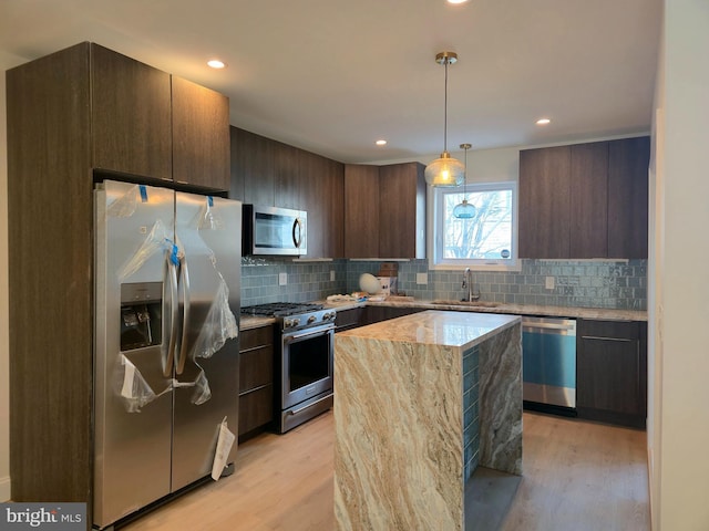 kitchen with a sink, stainless steel appliances, light wood-type flooring, and tasteful backsplash