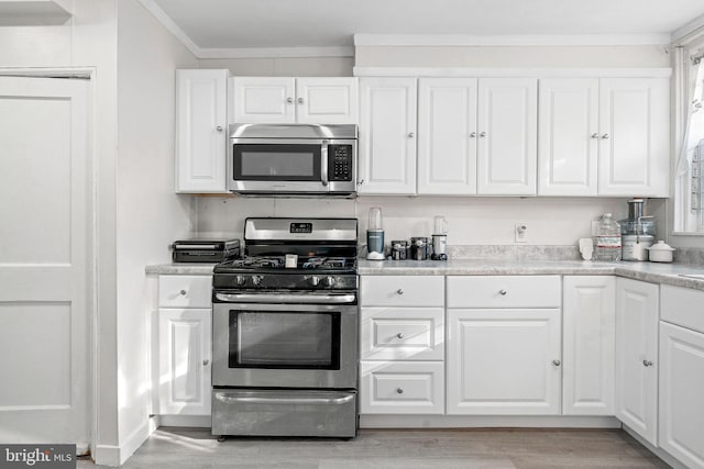 kitchen with light wood-type flooring, ornamental molding, white cabinets, and appliances with stainless steel finishes