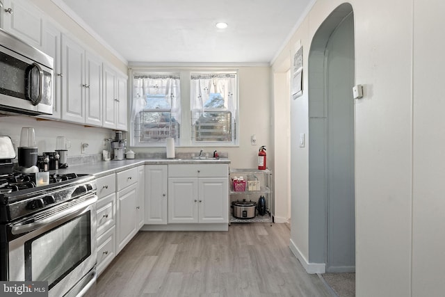 kitchen featuring ornamental molding, light hardwood / wood-style floors, white cabinets, and appliances with stainless steel finishes