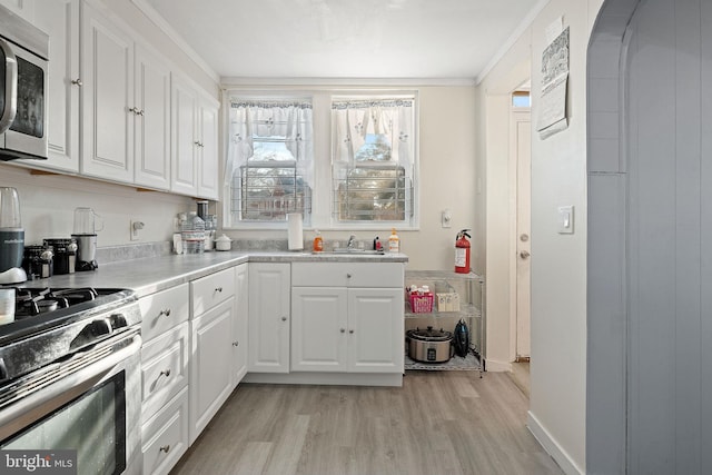 kitchen with appliances with stainless steel finishes, sink, light wood-type flooring, crown molding, and white cabinets